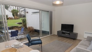 Un salon moderne comprenant un coin repas, un téléviseur à écran plat et une porte-fenêtre coulissante donnant sur un jardin.