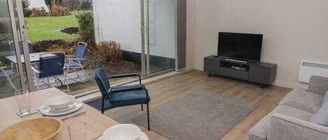 Una sala de estar moderna con comedor, un televisor de pantalla plana y una puerta corrediza de vidrio que da a un jardín.