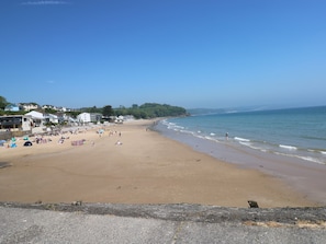 A wide sandy beach with a clear blue sky, a calm sea, and buildings along the coastline. - 14 Coedrath Park (Saundersfoot)