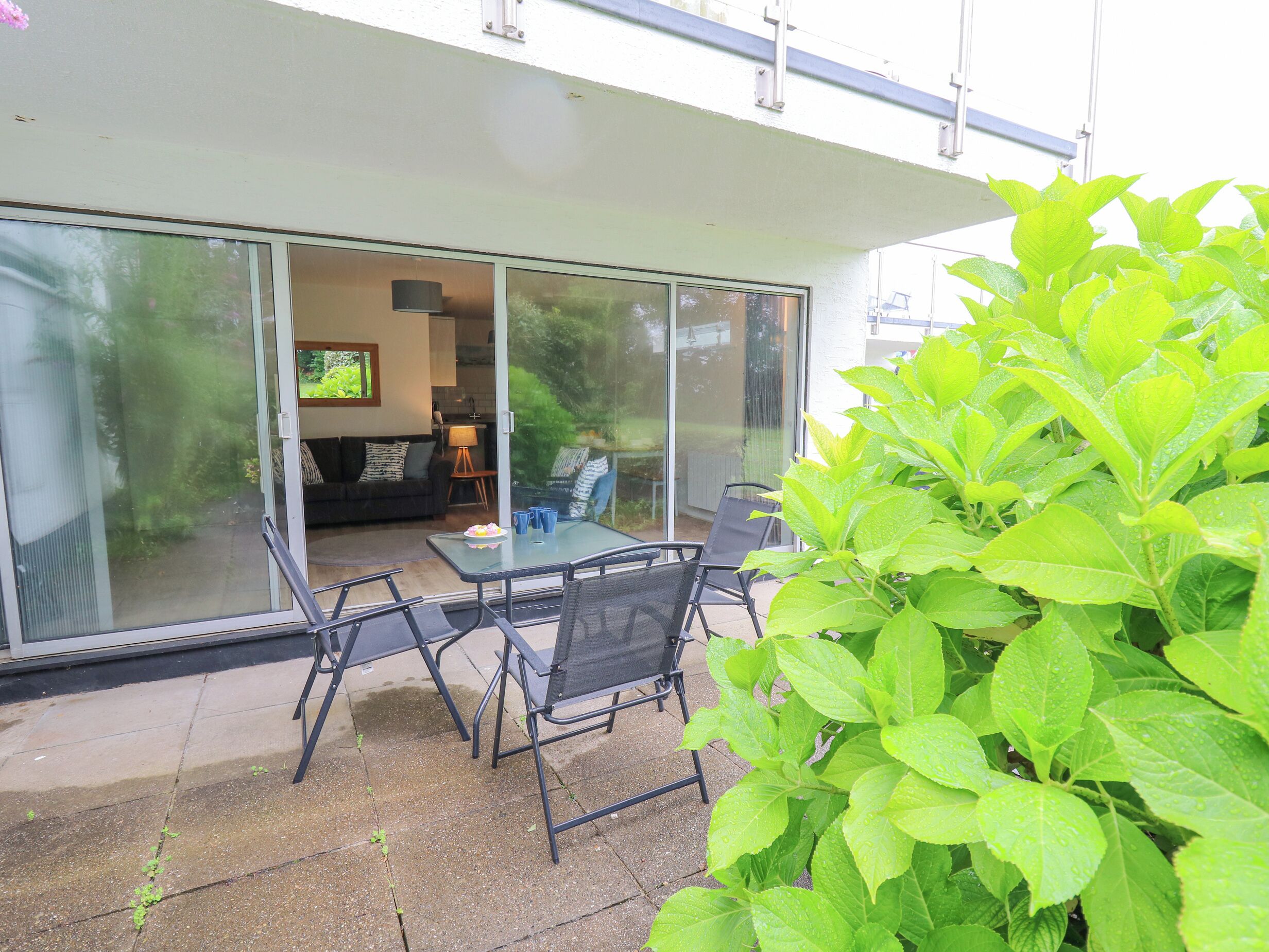 Eine Terrasse mit Glastür zu einem Wohnbereich, Gartenmöbel und einer Zimmerpflanze.