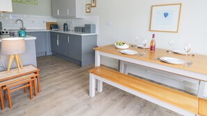 A modern kitchen with grey cabinets, a wooden dining table set with plates and wine glasses, and a bench.
