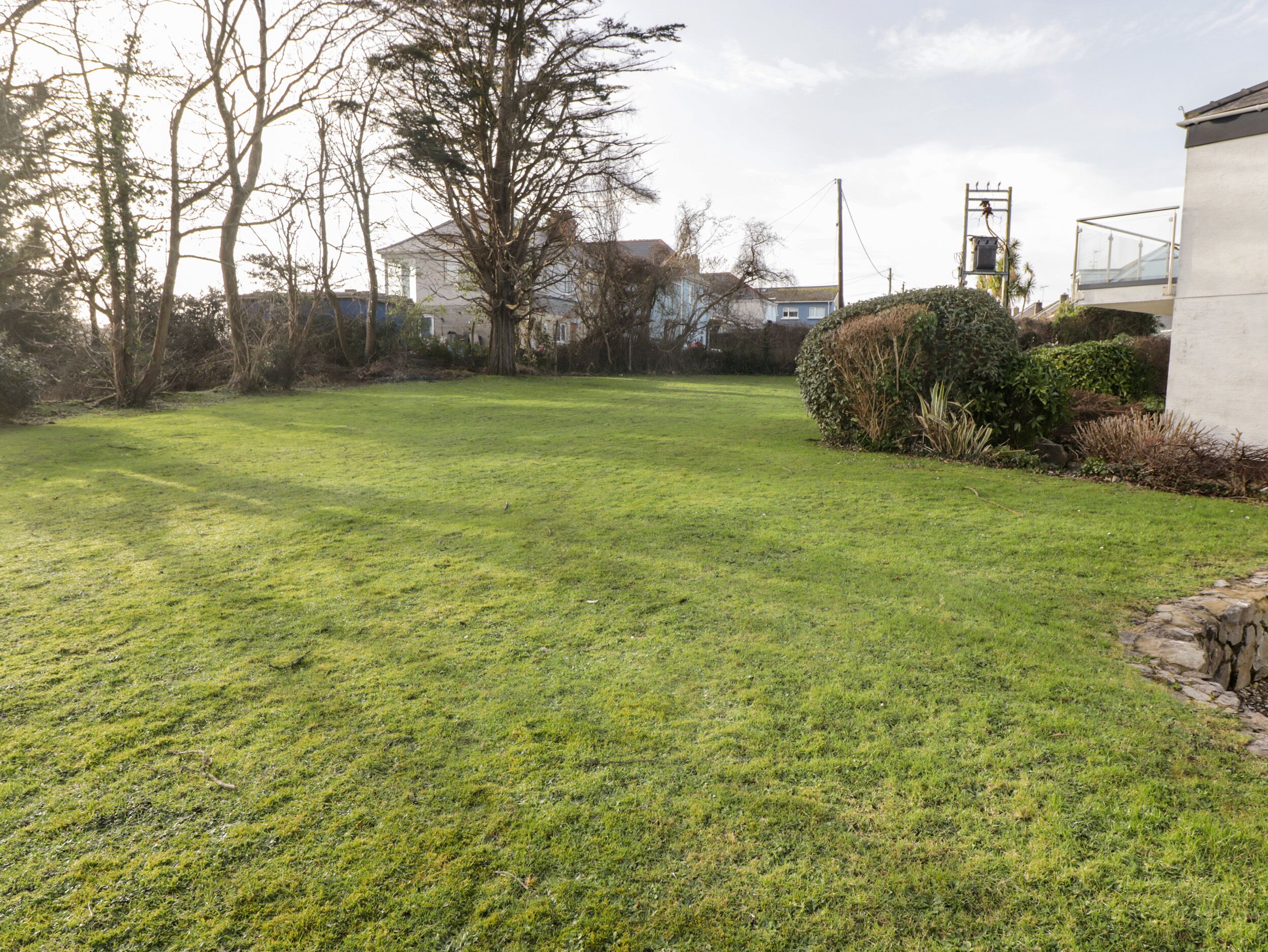 A grassy backyard with a house, trees, and a stone wall.