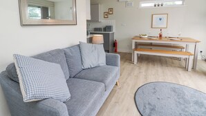 A modern living room with a grey sofa, a round rug, a wooden dining table, and a kitchen in the background.