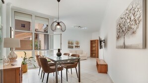 A modern living room with a glass dining table, brown chairs, a sofa, and a large window.