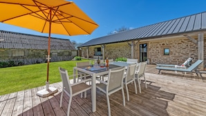 A wooden deck with a table and chairs, a yellow umbrella, and a stone building with a metal roof. - Holiday Home with Private Heated Pool, Private Terrace, Garden and Wi-Fi (Plouguerneau)