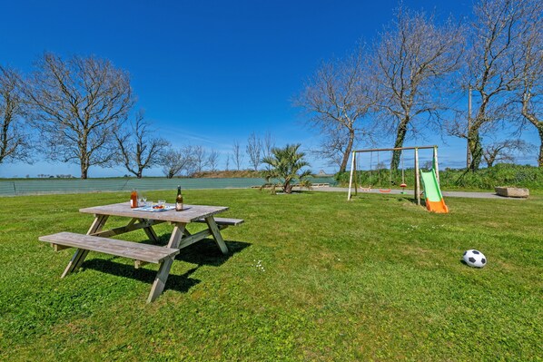 A picnic table with a bottle and a plate, a swing set, and a soccer ball on a grassy field.
