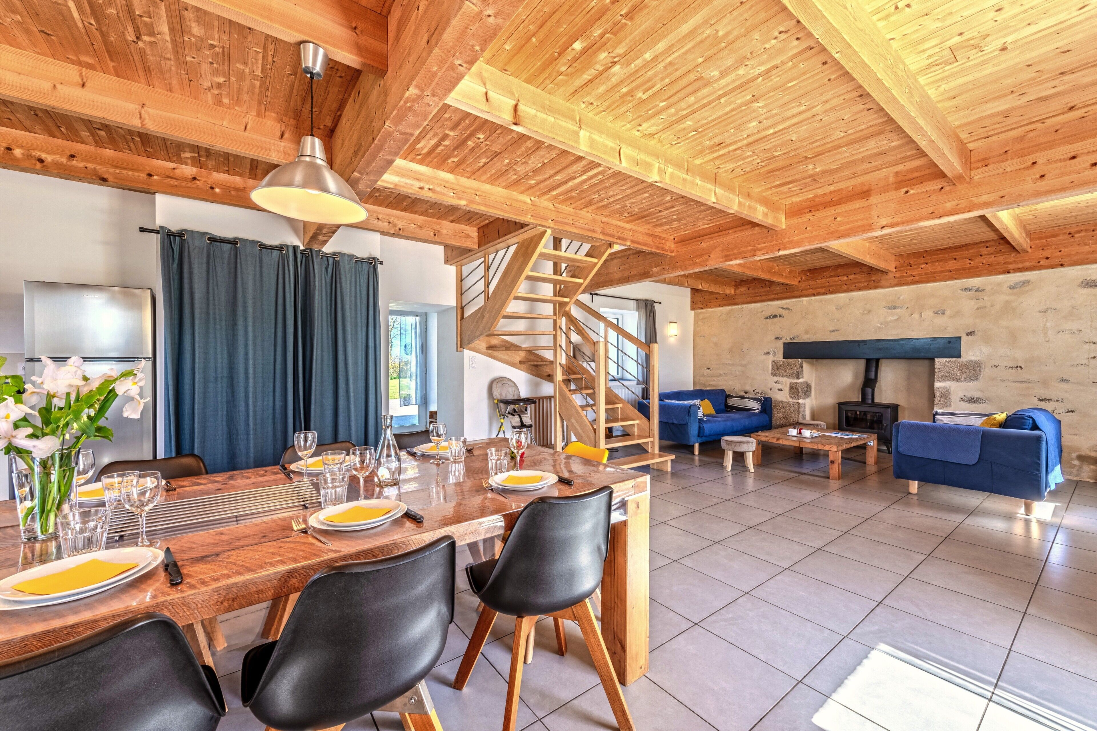 Un comedor con una mesa de madera preparada para cuatro personas, sillas negras y una escalera que sube a un nivel superior.