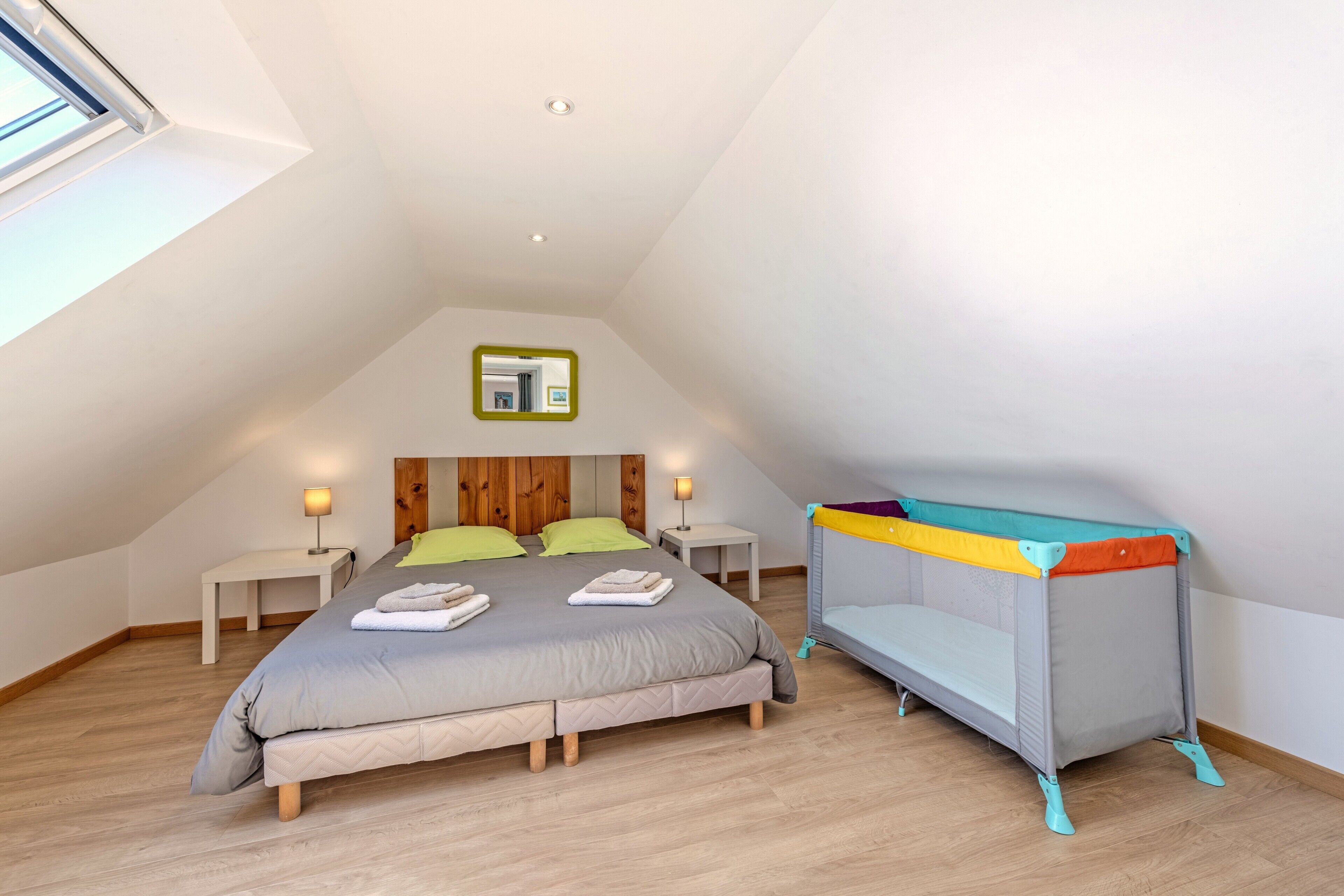 Een slaapkamer met een bed, een klein tafeltje, een nachtkastje, een stapelbed en een dakraam.