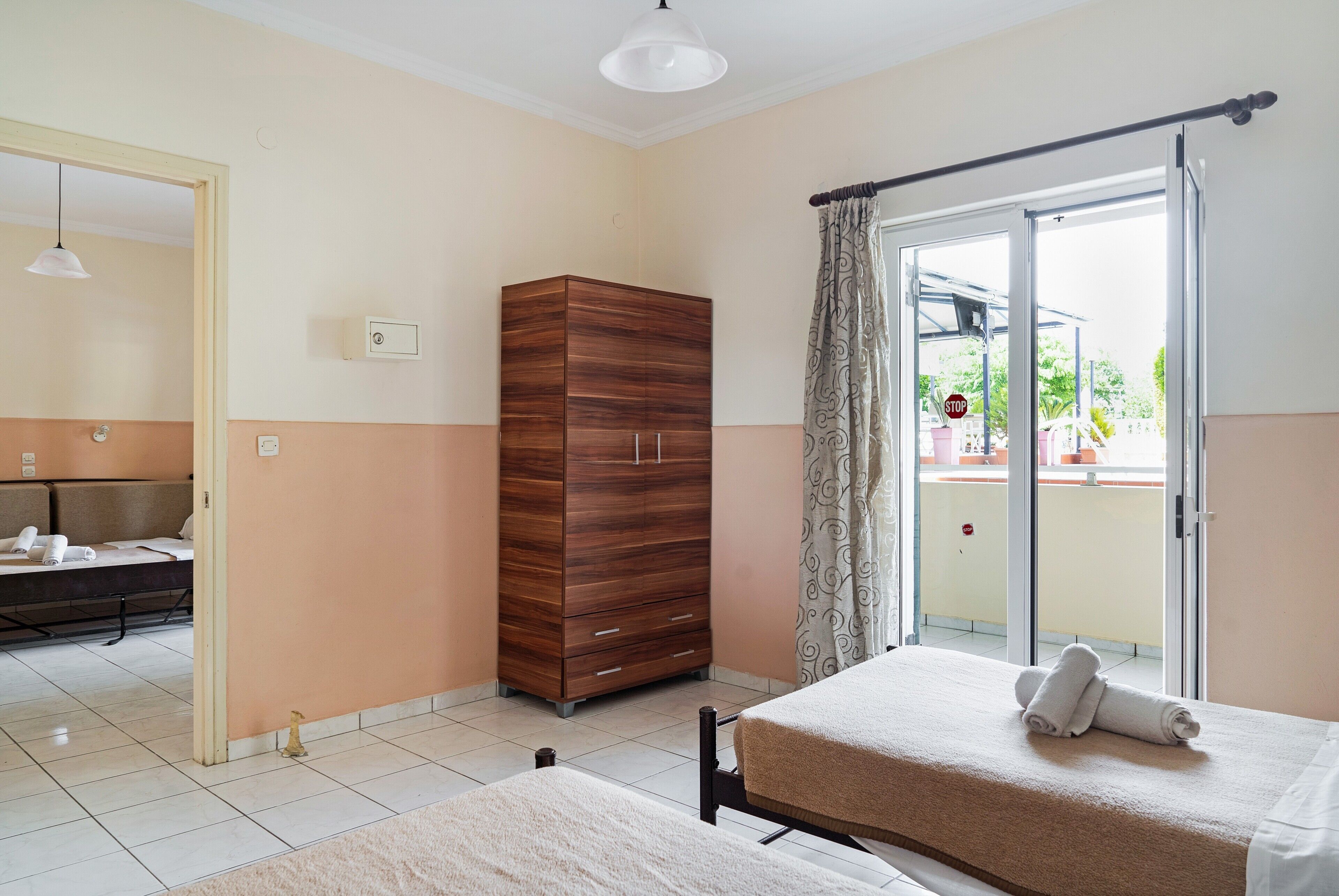 Hotellihuone, jossa on kaksi sänkyä, vaatekaappi, suihkulla varustettu kylpyhuone ja parveke, jolta on näkymä.