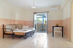 A room with a bed, a table, and a chair. There is a sliding door leading to an outdoor area with a table and chairs.