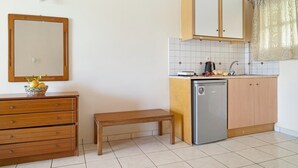 Eine kleine Küche mit Kühlschrank, Holzschränken, einer Bank und einer gefliesten Spritzschutzwand.