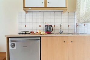 A kitchen with a dishwasher, a kettle, and a cutting board with vegetables.