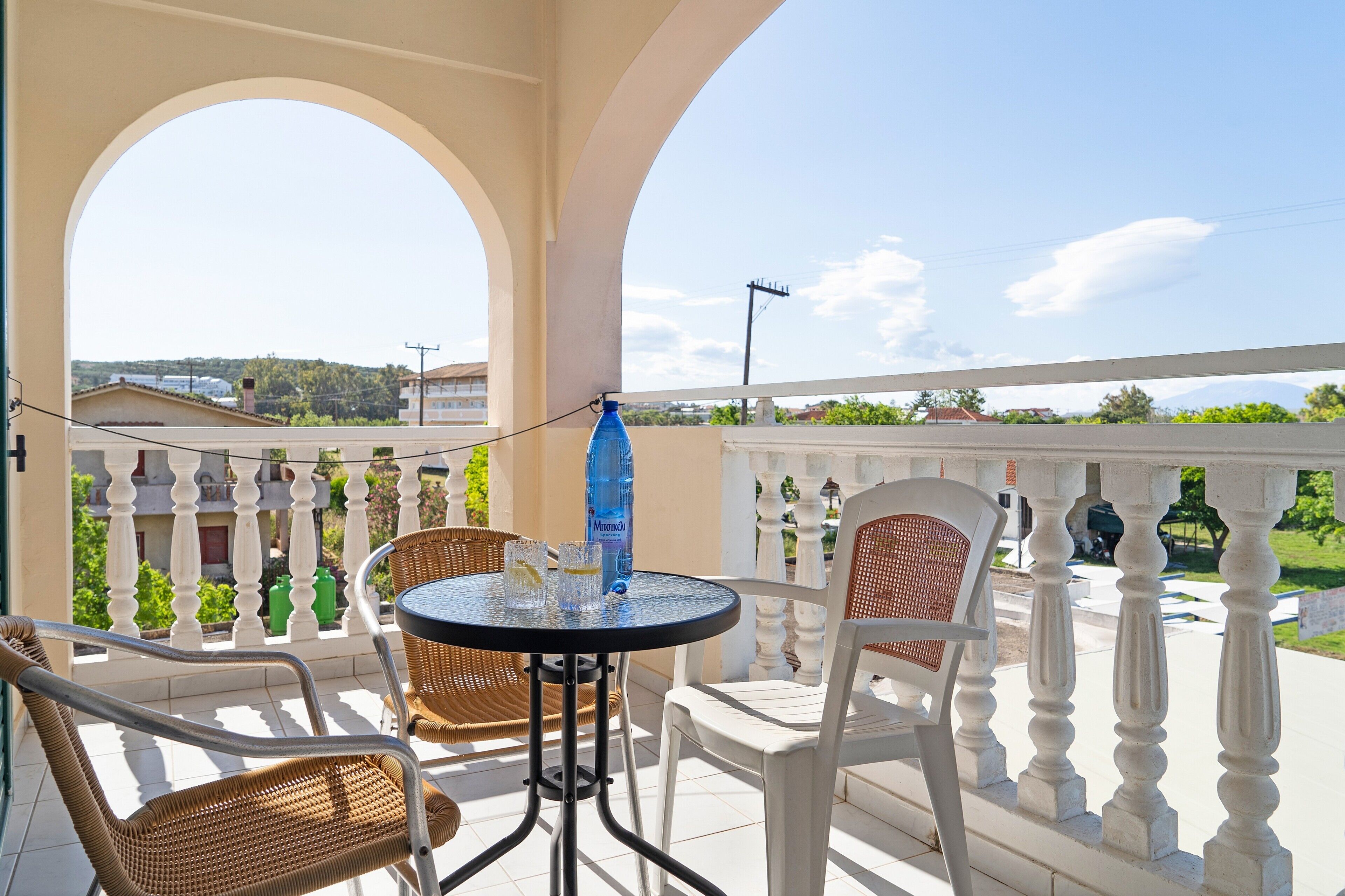 A balcony with a table and chairs, a blue water bottle, and a view of buildings and greenery.