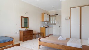 Een slaapkamer met twee bedden, een houten dressoir, een bureau en een kitchenette.