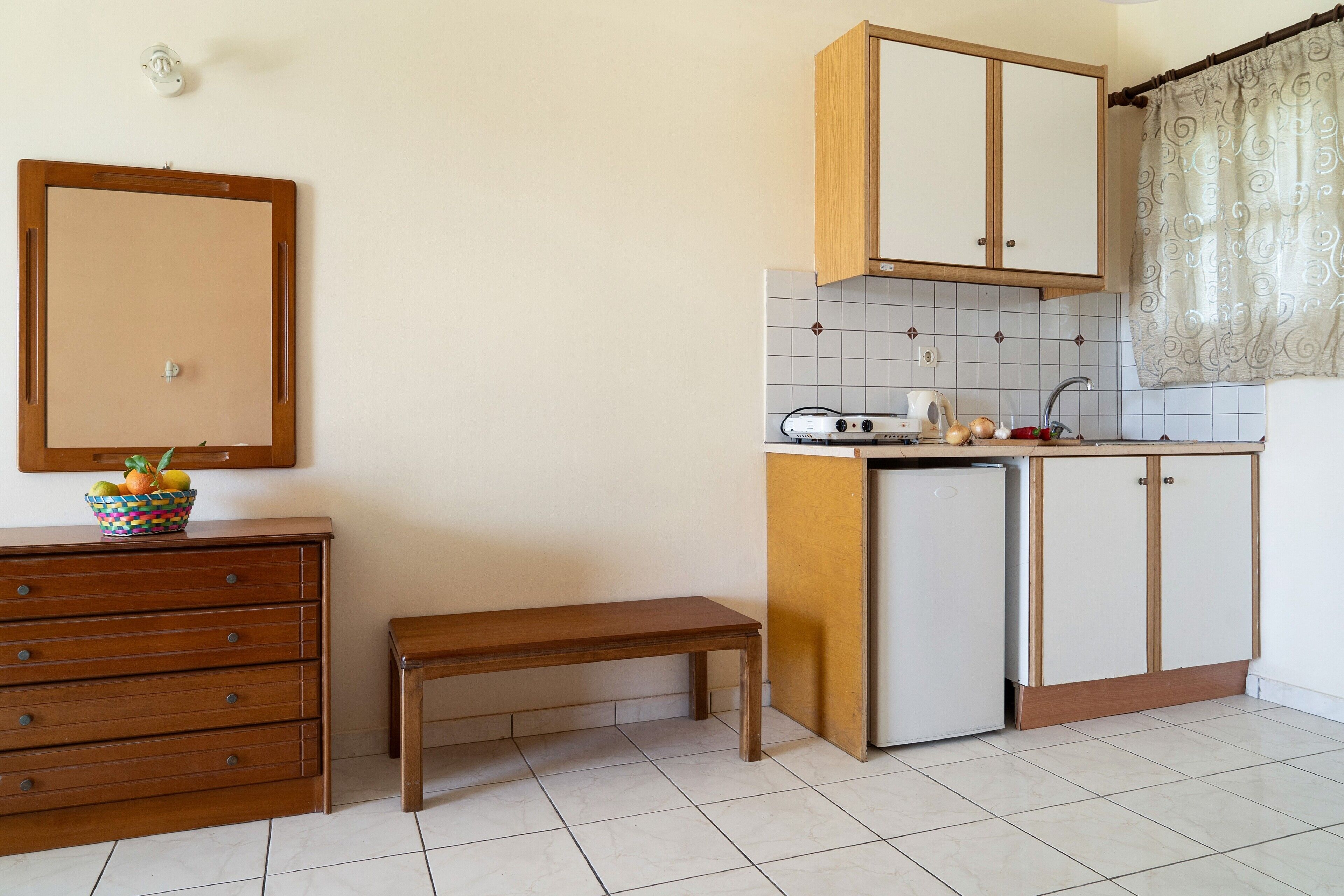Una cocina con un armario de madera, un refrigerador pequeño, una banca y un salpicadero de azulejos.