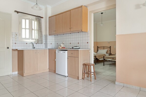 A kitchen with wooden cabinets, a dishwasher, a window with curtains, and a dining area with a table and chairs.