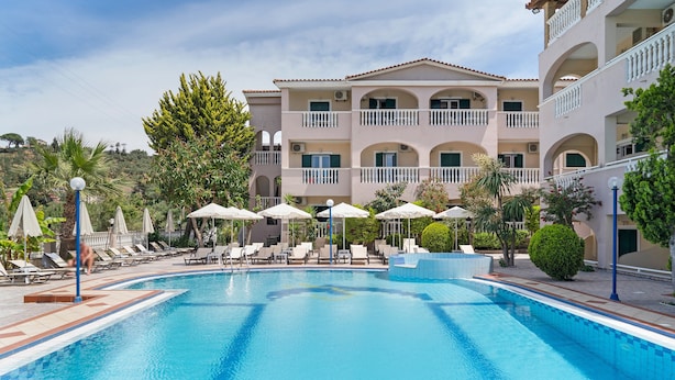 A swimming pool with lounge chairs and umbrellas, surrounded by a multi-story building with balconies. - Studio 'Sandy Maria Studio 503' with Shared Pool, Wi-Fi (Zante)