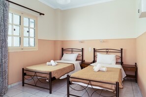 Una habitación de hotel con dos camas individuales, una ventana con cortinas, una mesita de noche y un enchufe de pared.