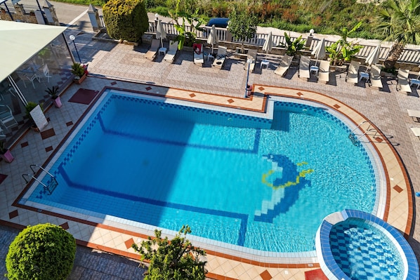 A swimming pool with lounge chairs and umbrellas, surrounded by a tiled deck and greenery.
