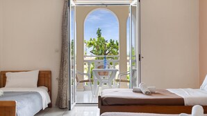 Camera d'albergo con due letti, un balcone con tavolo e sedie e vista sugli alberi.