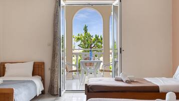 Habitación de hotel con dos camas, un balcón con mesa y sillas, y vista a árboles.