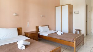 Camera d'albergo con due letti singoli, un armadio in legno, un comodino e un interruttore della luce fissato al muro.