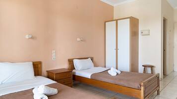 Habitación de hotel con dos camas individuales, un armario de madera, una mesita de noche pequeña e interruptor de luz en la pared.