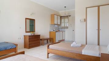 Een slaapkamer met twee bedden, een houten dressoir, een bureau en een kitchenette.
