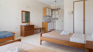 Une chambre avec deux lits, une commode en bois, un bureau, un miroir et un coin cuisine.
