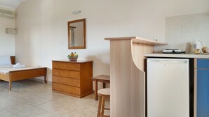 A bedroom with a bed, a wooden dresser, a small table, and a kitchenette area with a refrigerator. - Studio 'Sandy Maria Studio 402' with Shared Pool, Wi-Fi (Zante)