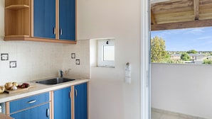 A kitchen with blue cabinets, a sink, and a window overlooking a residential area. - Studio 'Sandy Maria Studio 402' with Shared Pool, Wi-Fi (Zante)