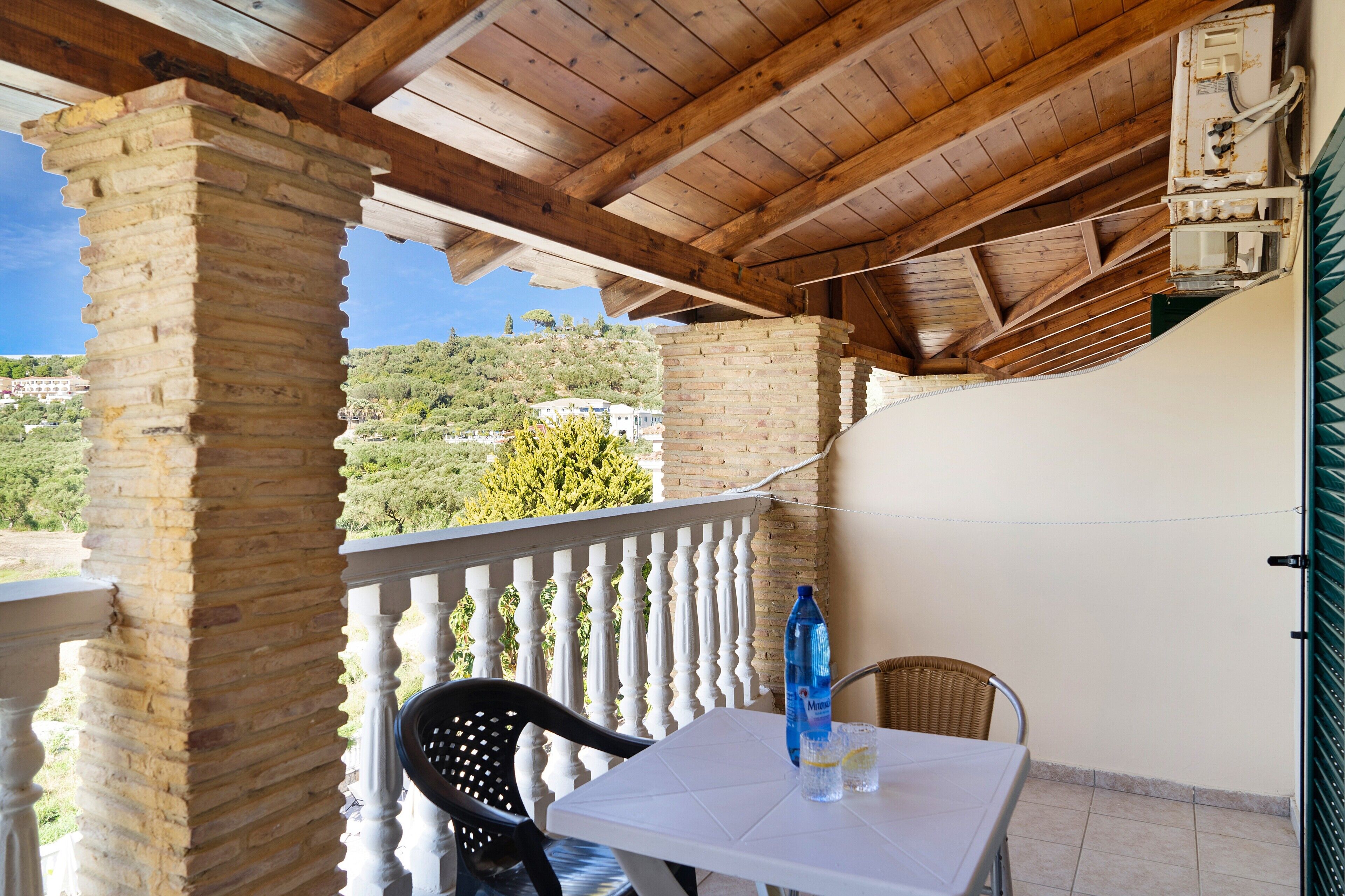 Un balcon abrité avec une table, des chaises et une bouteille d’eau.