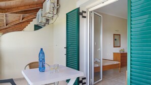 Une pièce avec un lit, une table sur laquelle se trouvent une bouteille et des verres, une chaise en osier et un escalier.