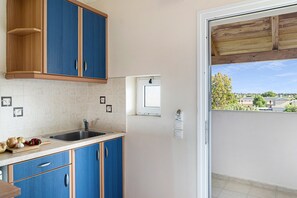 Een keuken met blauwe kastjes, een spoelbak en een raam met uitzicht op een woonwijk.