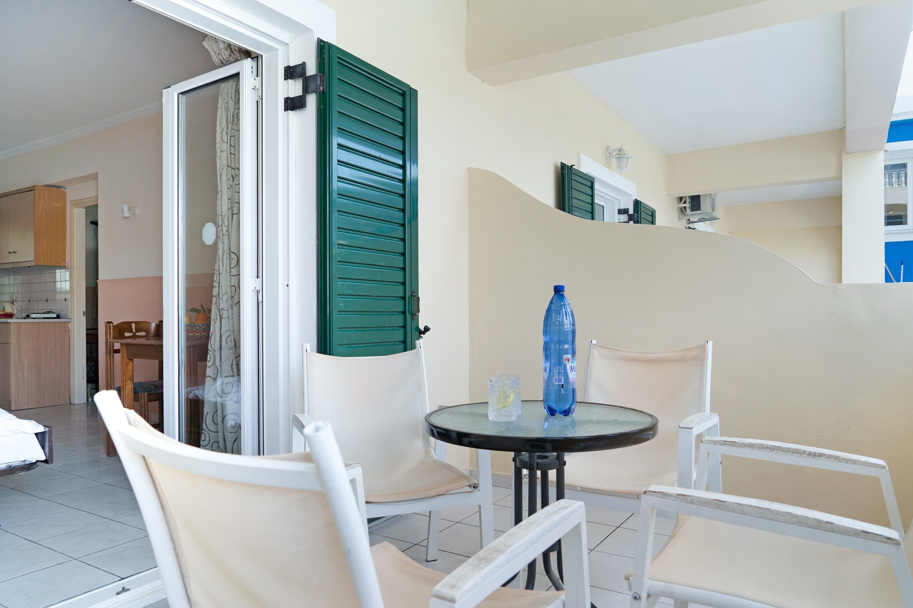 Quarto com mesa de jantar, cadeiras, área de cozinha e porta deslizante com portaria verde.