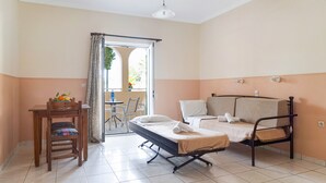 A single bed with a mattress, a wooden chair, a small table with a fruit bowl, and a view through an open door. - Studio 'Sandy Maria Studio 504' with Shared Pool, Wi-Fi  (Zante)