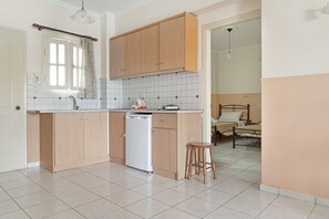 A kitchen with wooden cabinets, a dishwasher, a window with curtains, and a dining area with a table and chairs.