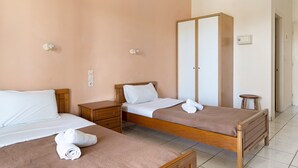 Een hotelkamer met twee eenpersoonsbedden, een houten garderobe, een nachtkastje en een klein krukje.