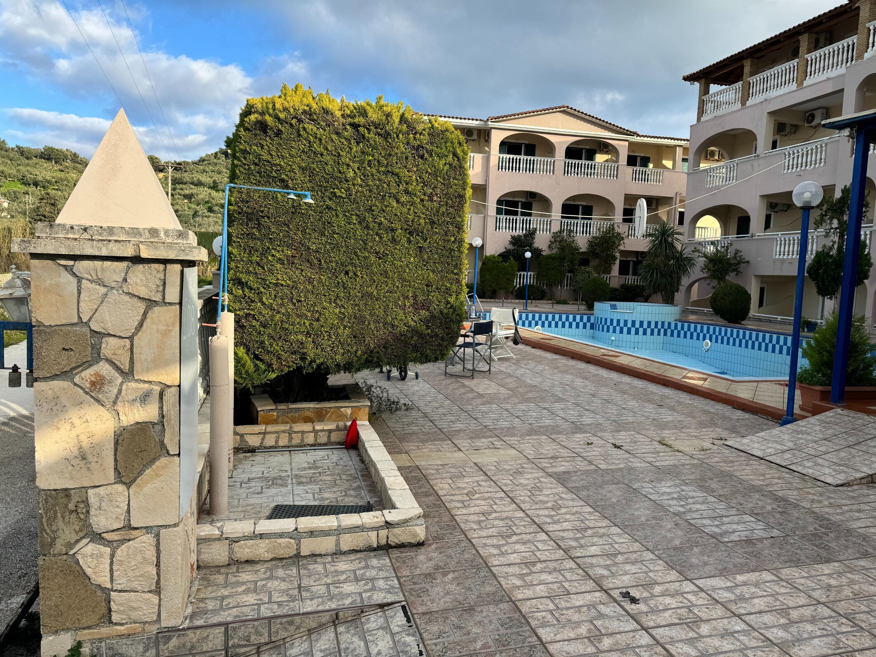 Une construction en pierre, un arbuste taillé avec soin, une piscine et un immeuble à plusieurs étages doté de balcons.