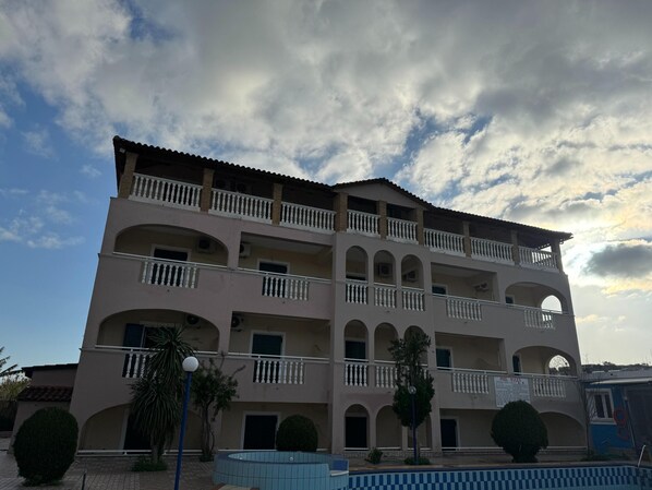 A multi-story building with balconies, a swimming pool, and a clear sky.