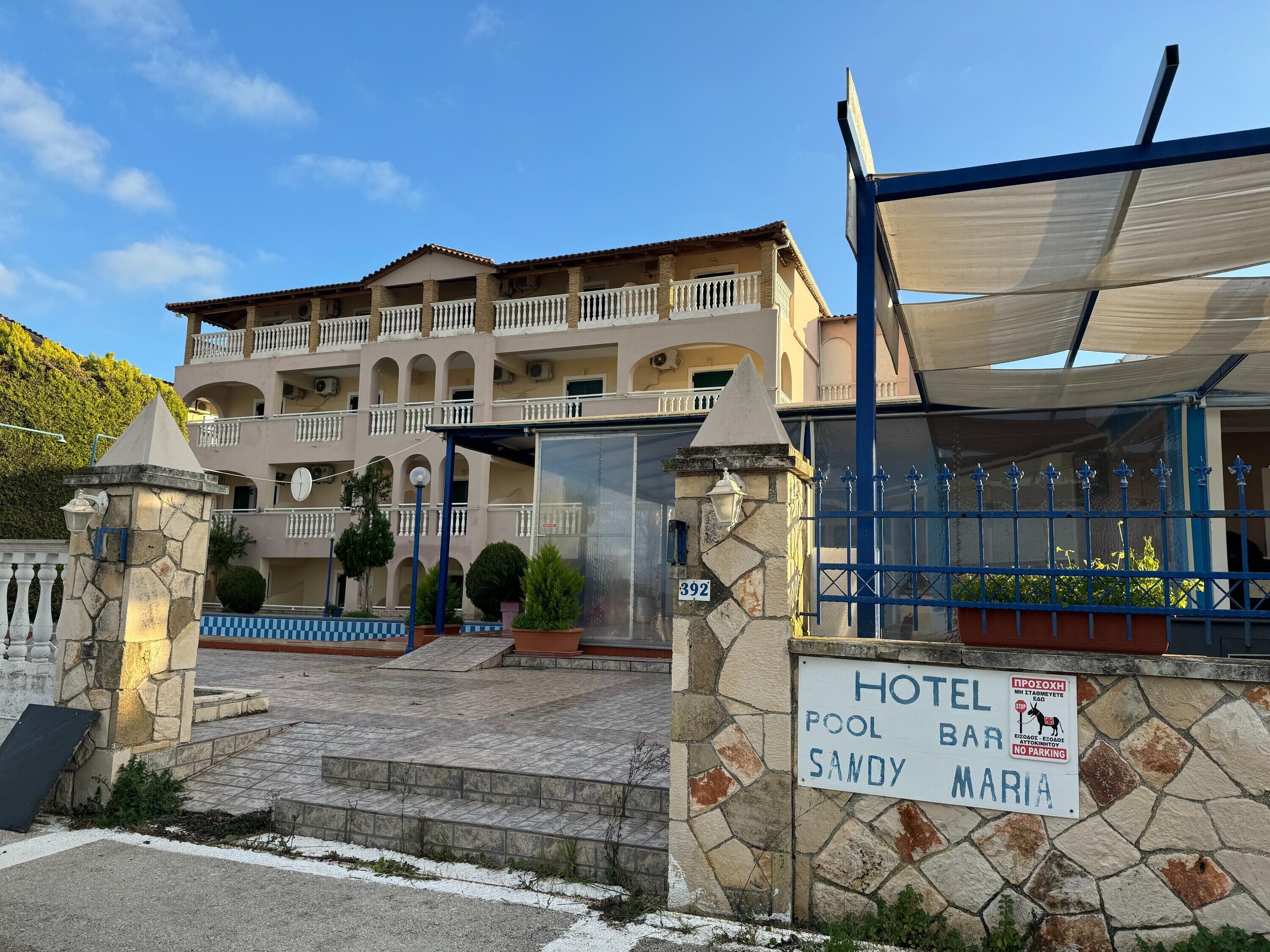 A hotel with a pool bar named Sandy Maria, stone walls, and a blue gate.