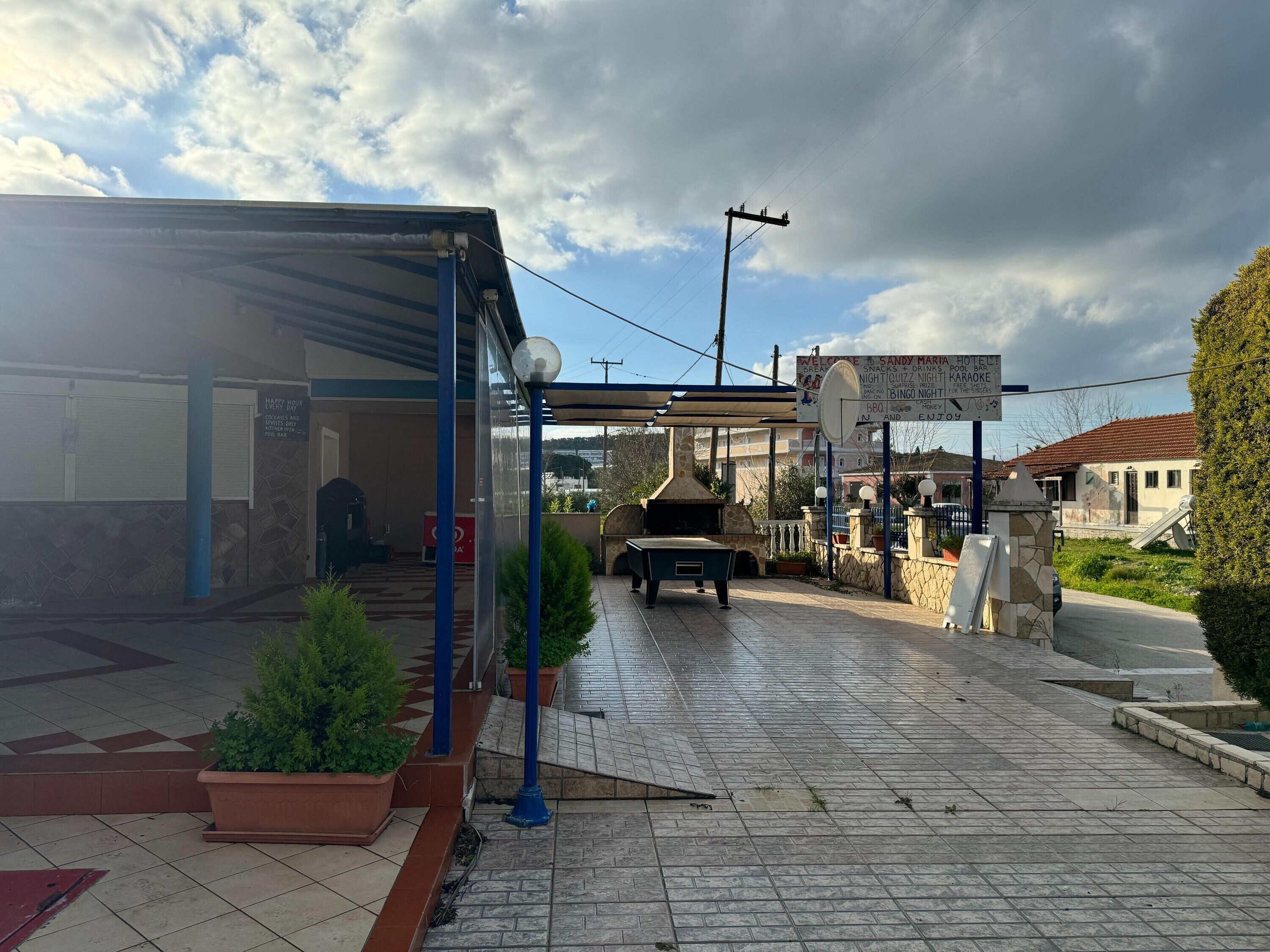 L’entrée d’un hôtel, avec un espace extérieur abrité, un barbecue et un panneau indiquant les services offerts par l’hôtel.