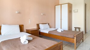Une chambre d’hôtel avec deux lits, une armoire, une table de chevet et un petit tabouret.