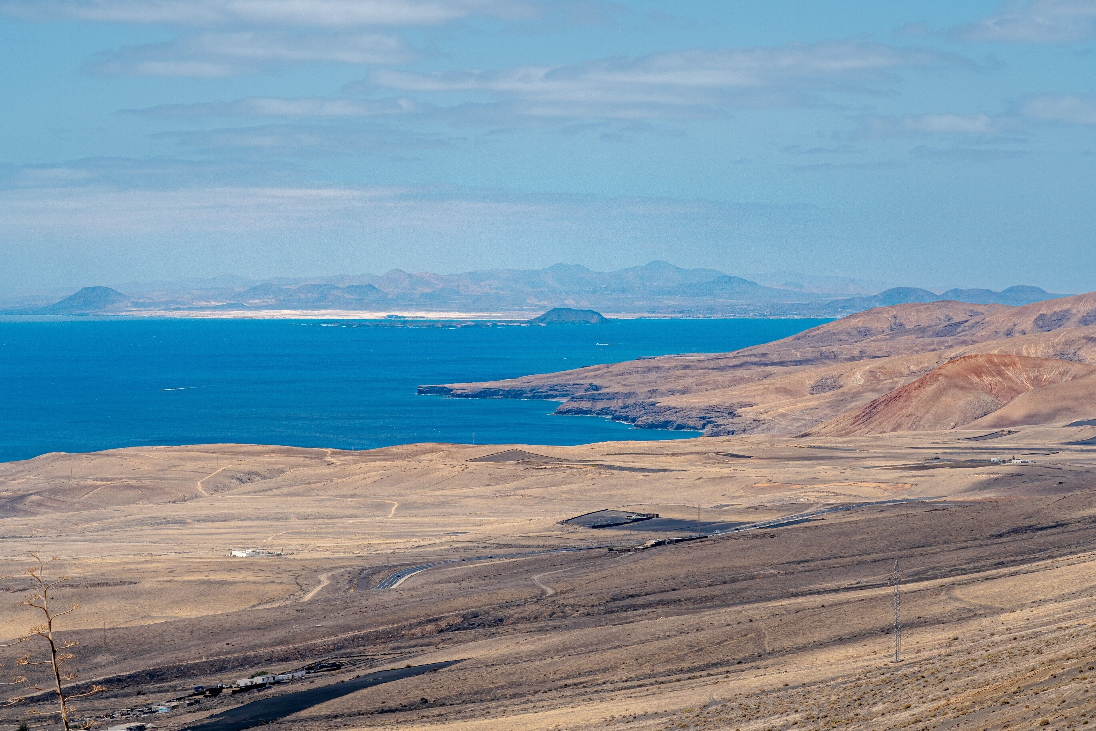 Un paysage côtier offrant une vue dégagée sur la mer, des montagnes lointaines et un terrain aride.