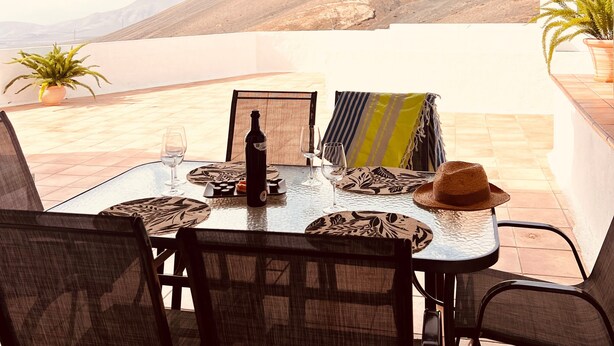An outdoor dining area with a table set for two, overlooking a mountainous landscape.