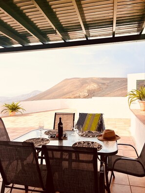 Un espacio exterior para comer con una mesa dispuesta para dos, con vistas a un paisaje montañoso.