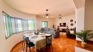 A dining area with a round table, chairs, and a sofa in the background.