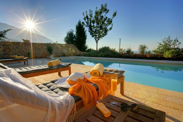 Un espace aménagé au bord de la piscine, avec des chaises longues, une table et un mur en pierre.