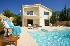 Un bâtiment à deux étages doté d’une piscine, de chaises longues et d’un mur en pierre.