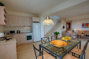 Une cuisine moderne dotée d’appareils électroménagers intégrés, un coin repas avec une table en verre et un escalier menant à une mezzanine.